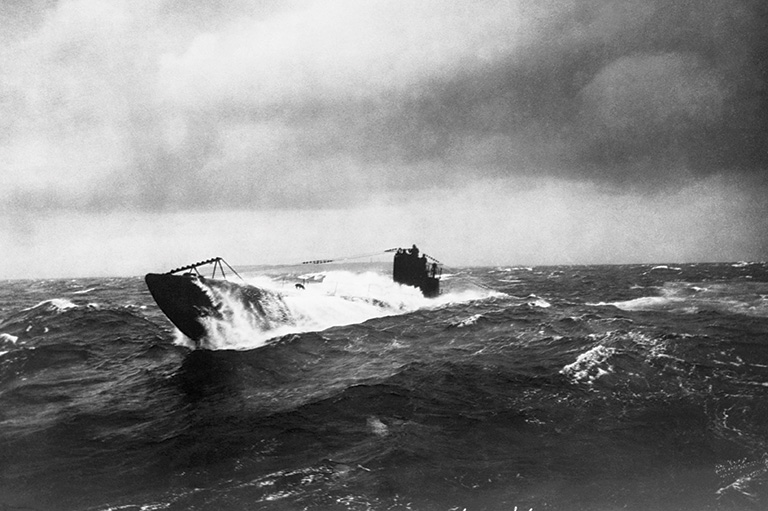 This is a gray scale image that shows a u-boat emerging from a dark body of water. 