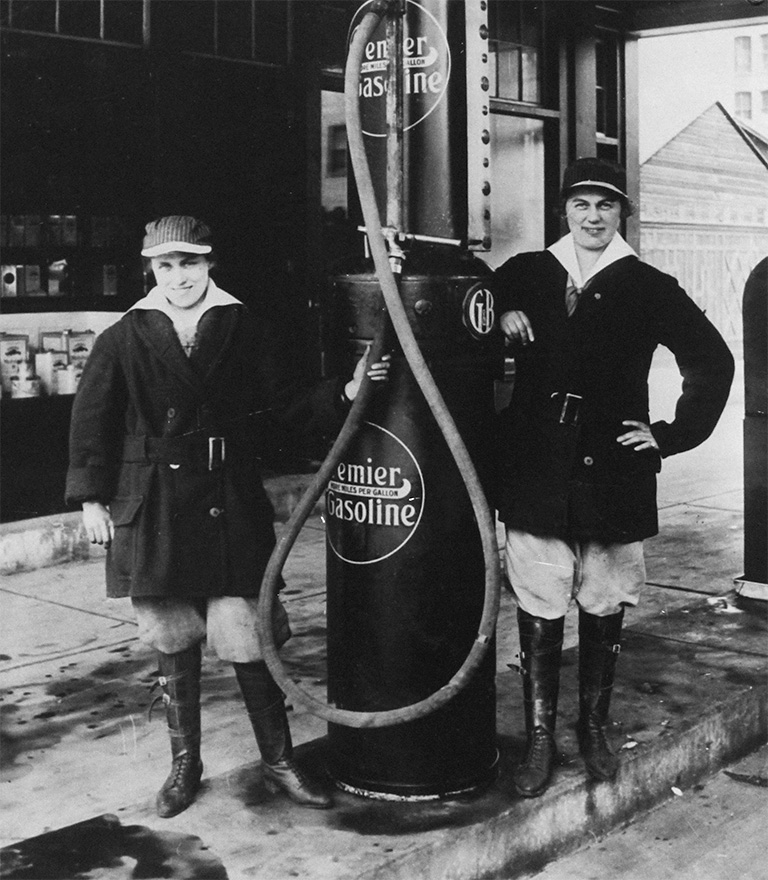 Two women stand beside a gas pump.