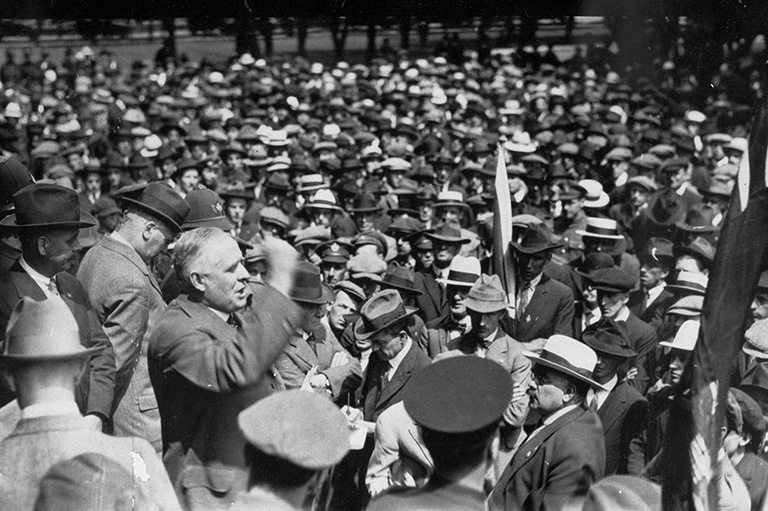 A crowd of people surrounding a man who is talking to them. 